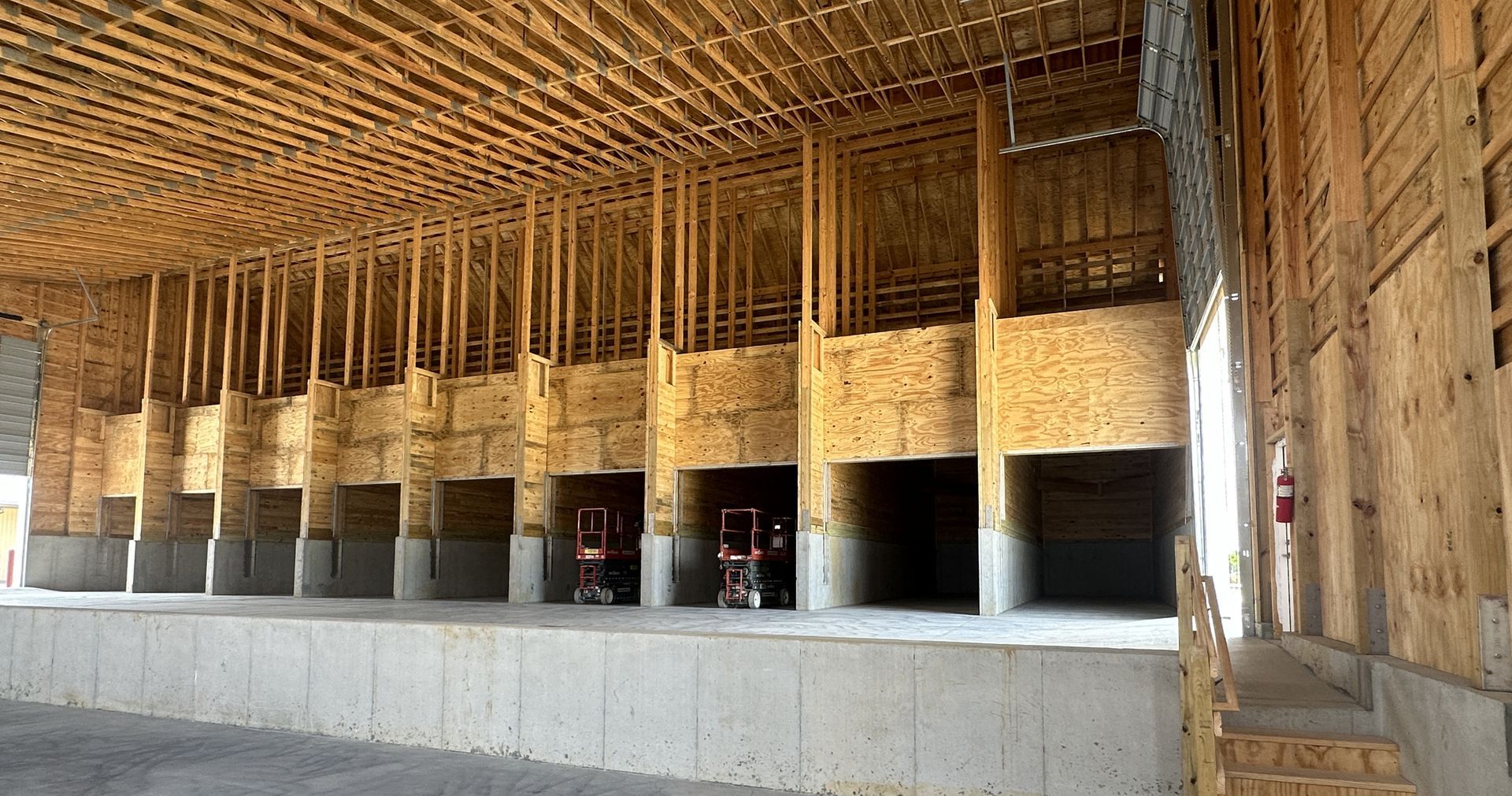 Construction site interior: wooden framing and concrete stage, open bays with workers.