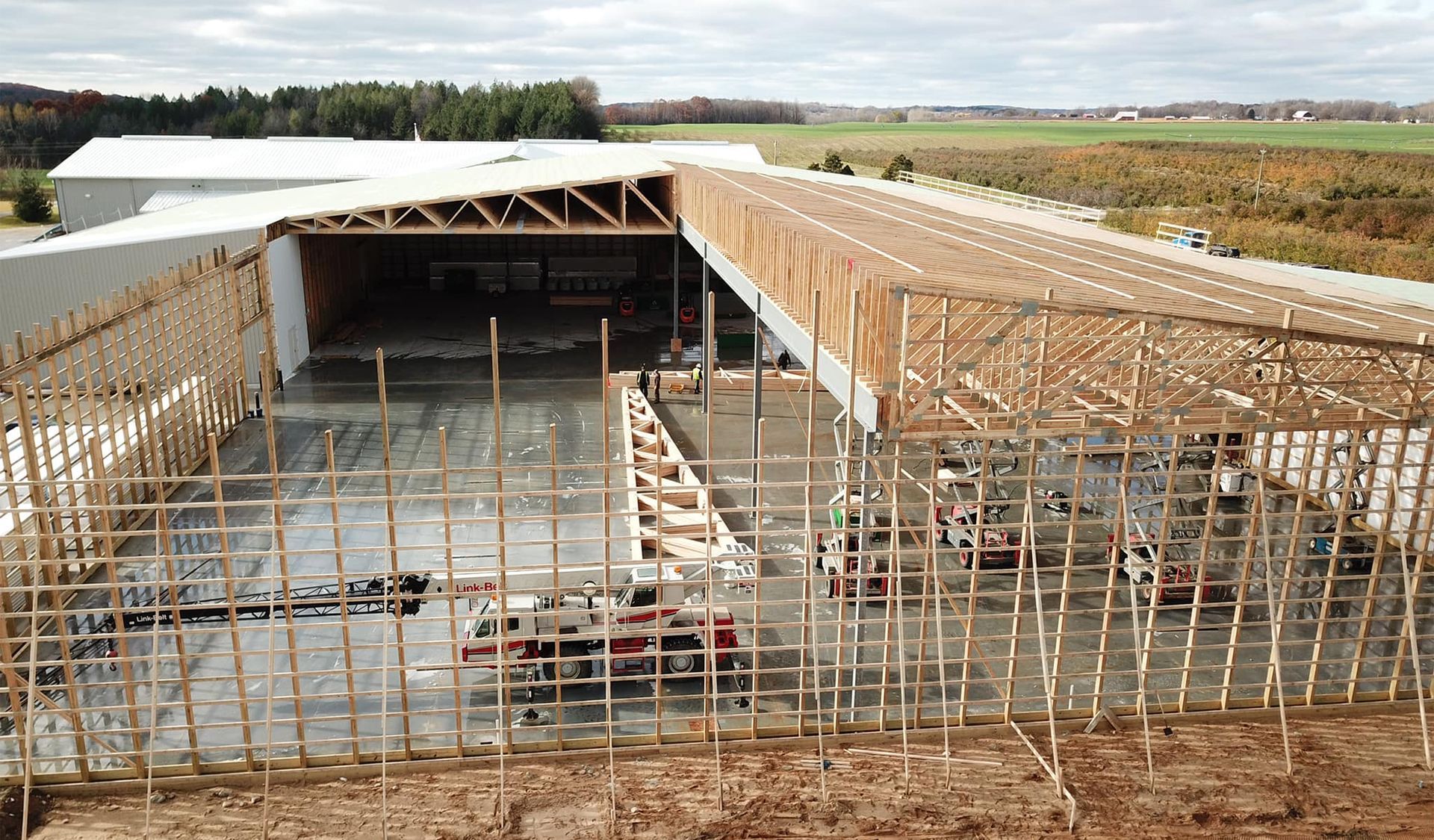 Building under construction; wooden frame and concrete foundation with large open space, outdoors.