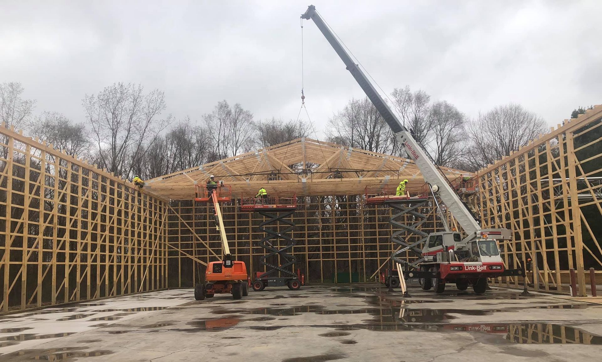 Construction site: Wooden structure with workers, crane, and lift under overcast sky.