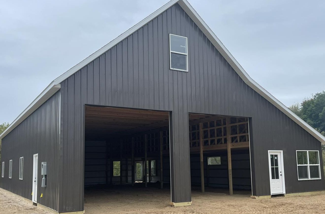 Dark gray barn with two open bays and white trim under a cloudy sky.