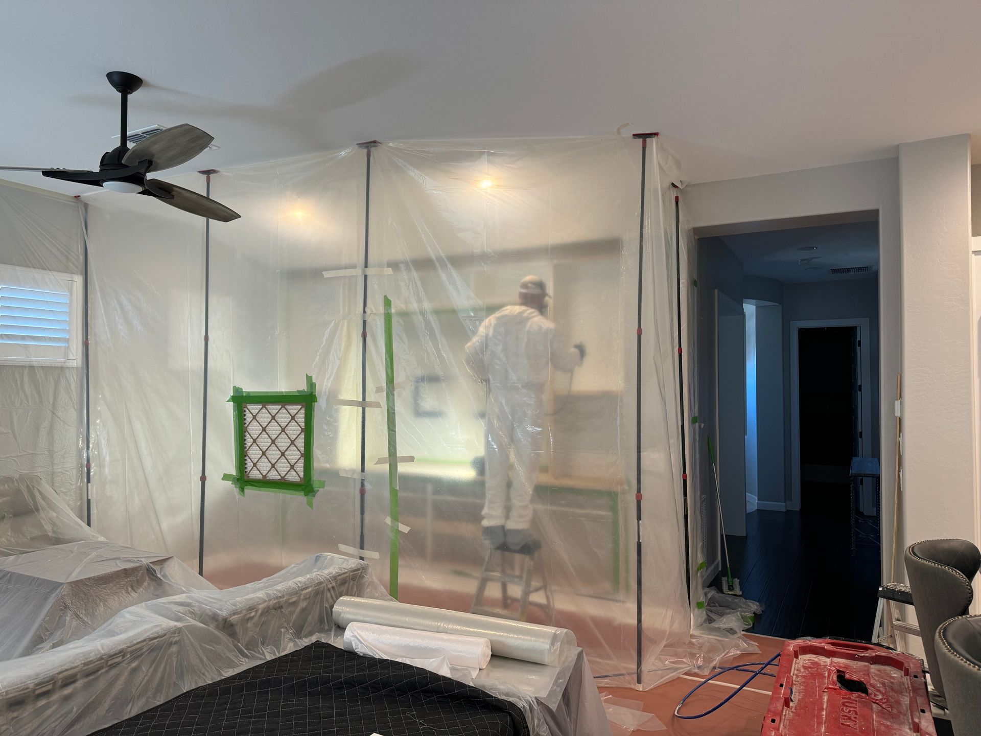 A man is standing on a ladder in a room covered in plastic.
