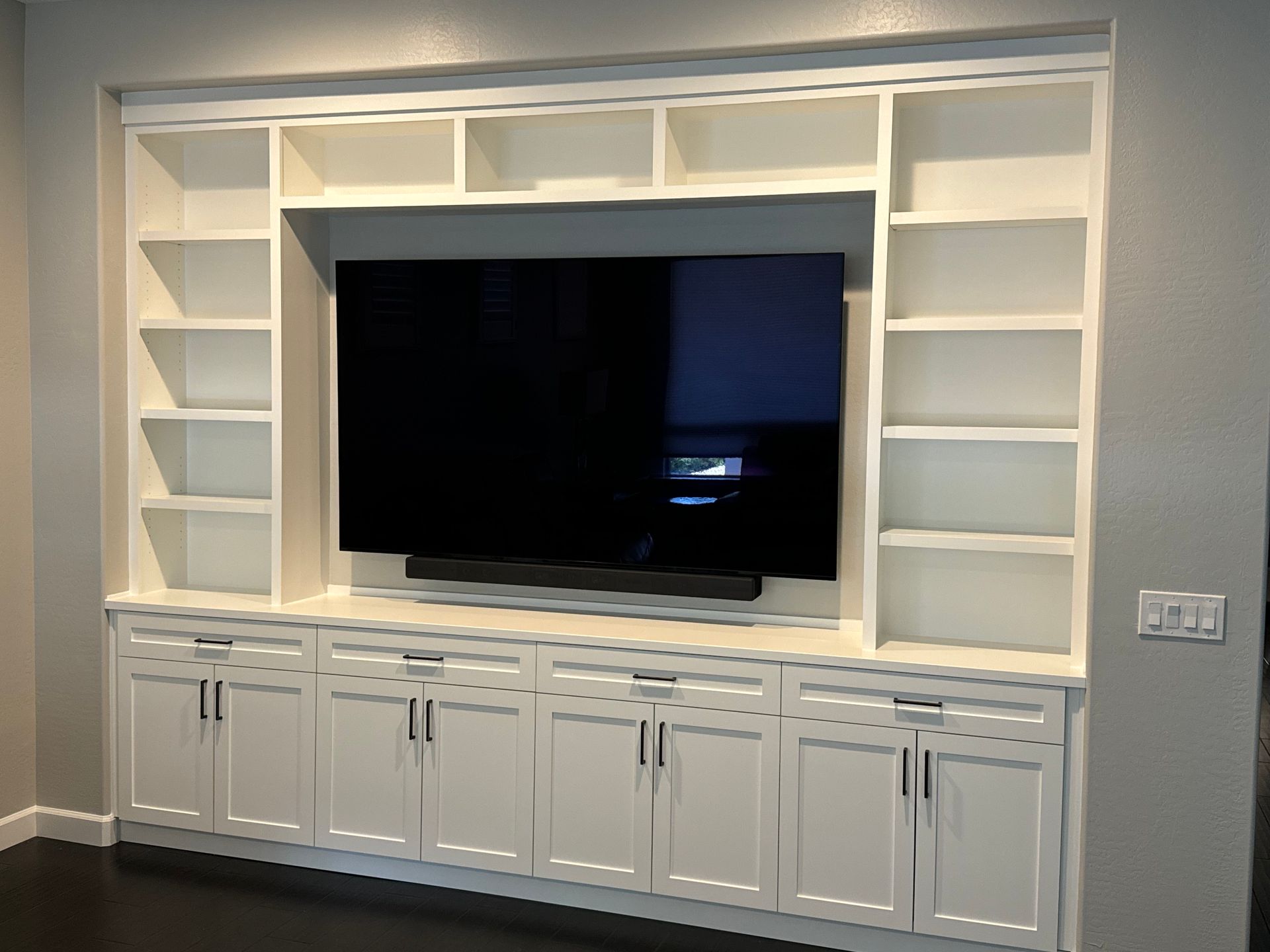 A living room with white cabinets , shelves and a flat screen tv.
