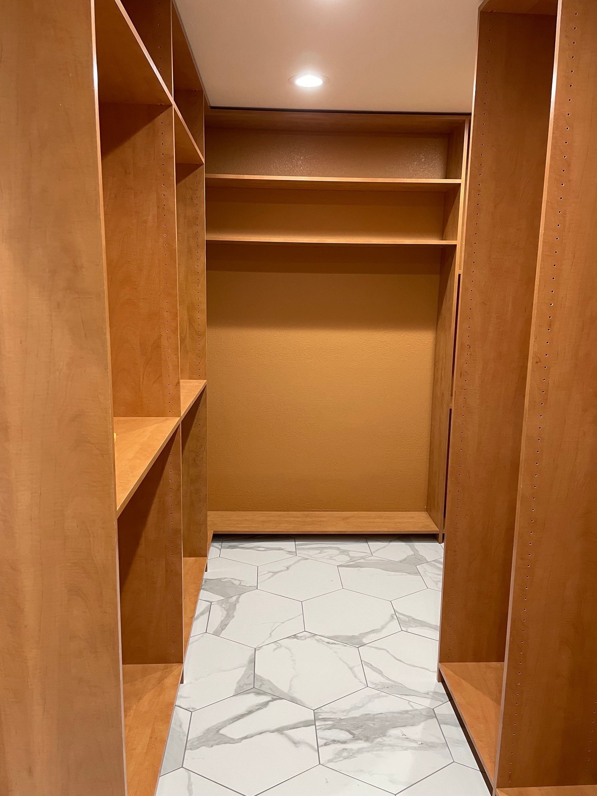 A walk in closet with wooden shelves and a marble floor.