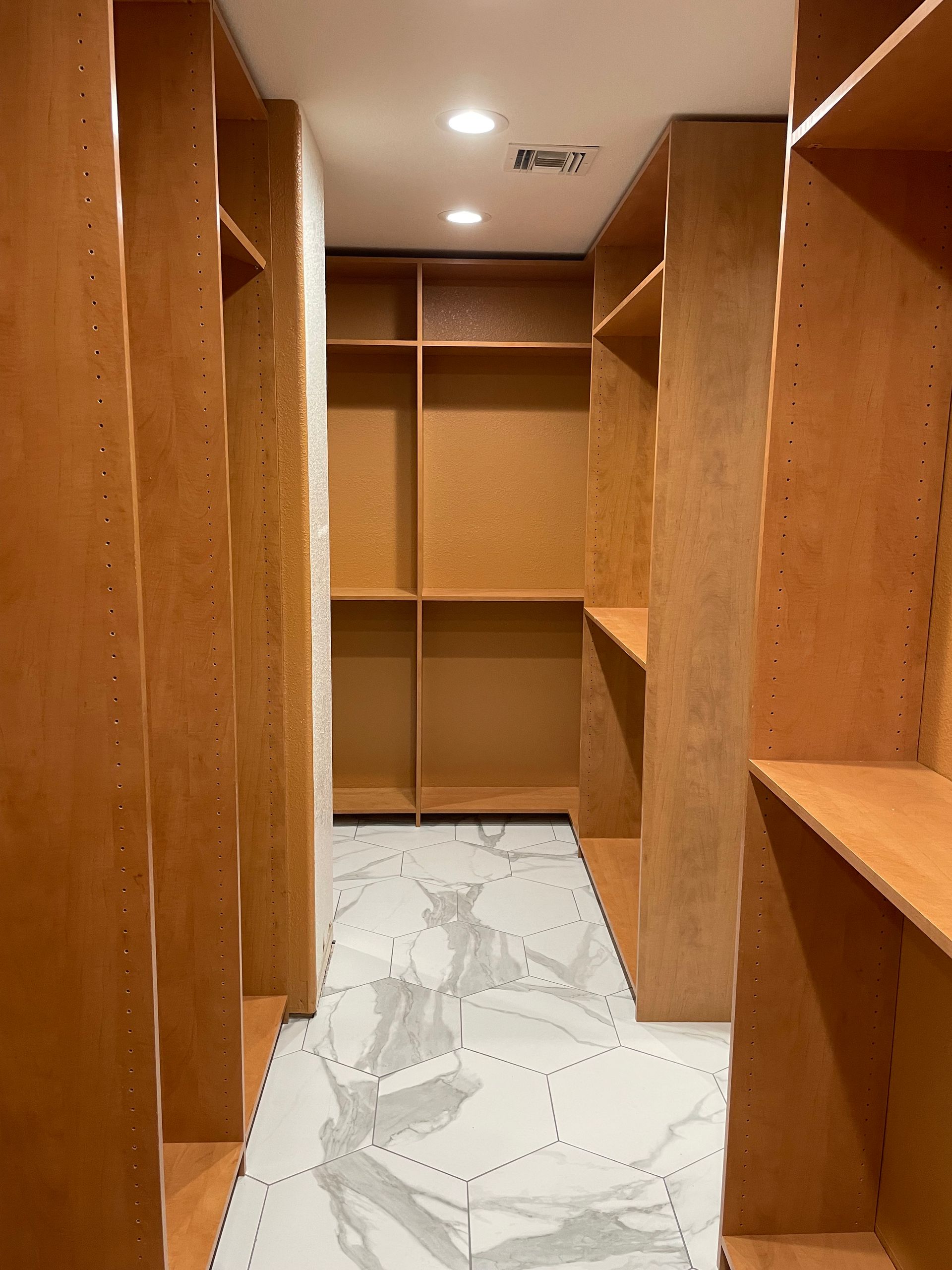 A walk in closet with wooden shelves and marble floors