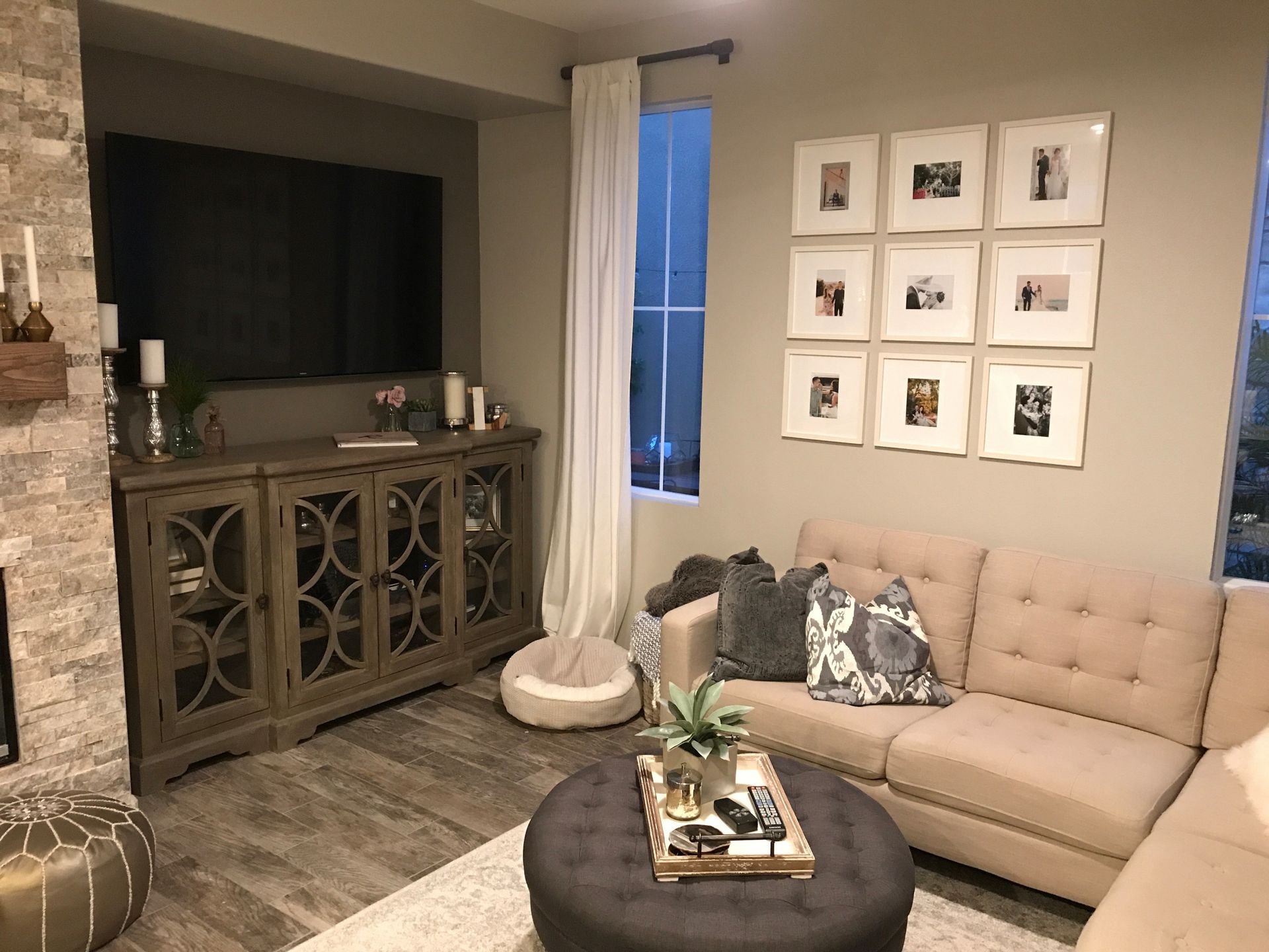 A living room with a couch , ottoman , television and pictures on the wall.