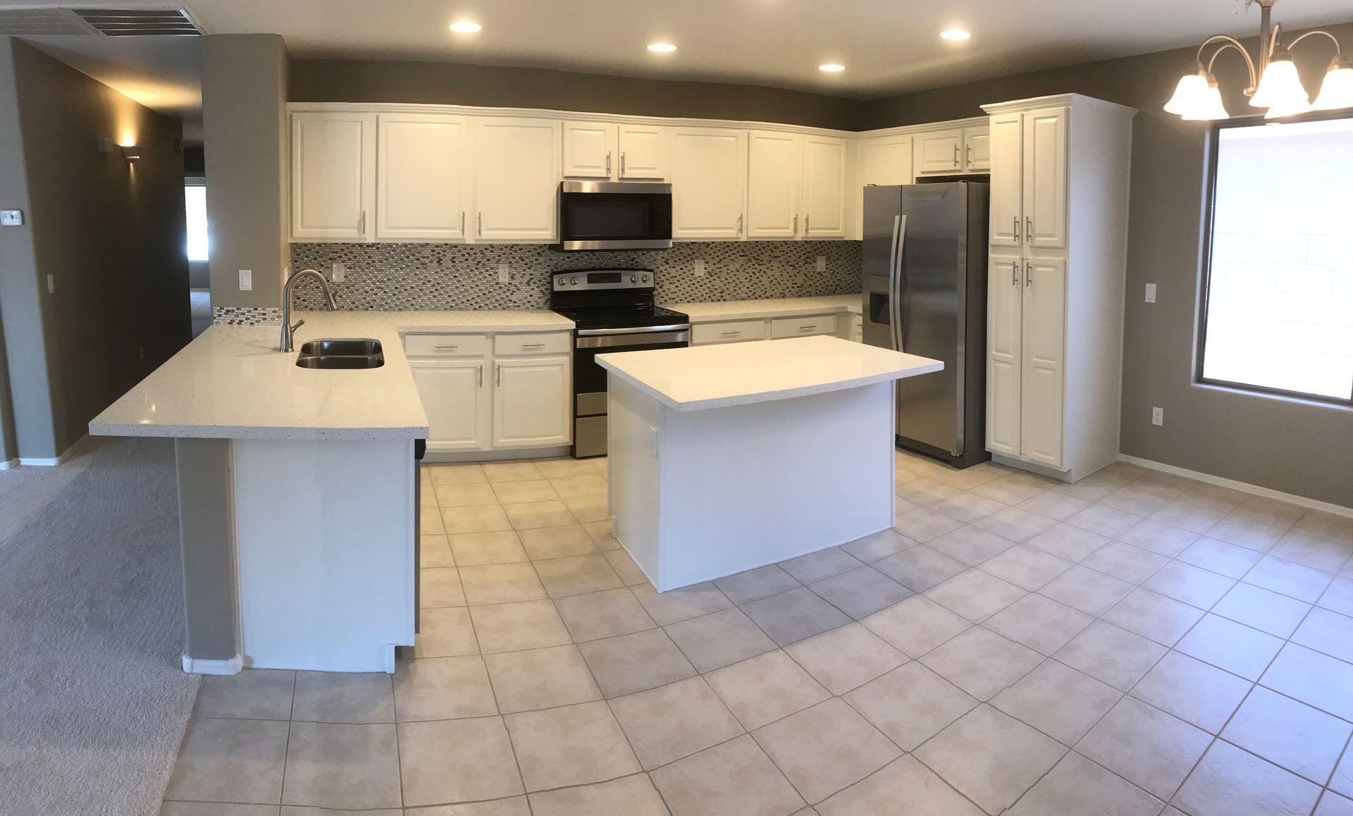 An empty kitchen with white cabinets and stainless steel appliances