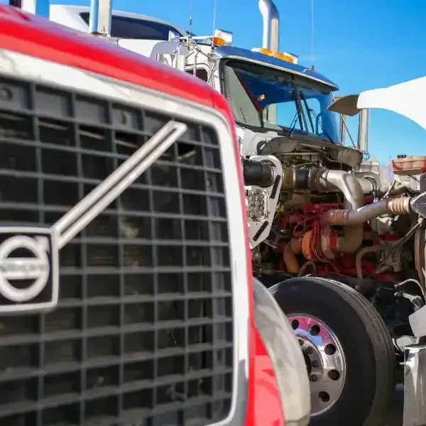 Red Volvo truck grill close up with a second truck's exposed engine in the background. Blue sky.