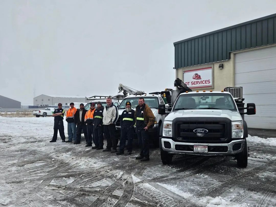 Group of people in work attire pose with tow trucks in a snowy environment in front of a building.
