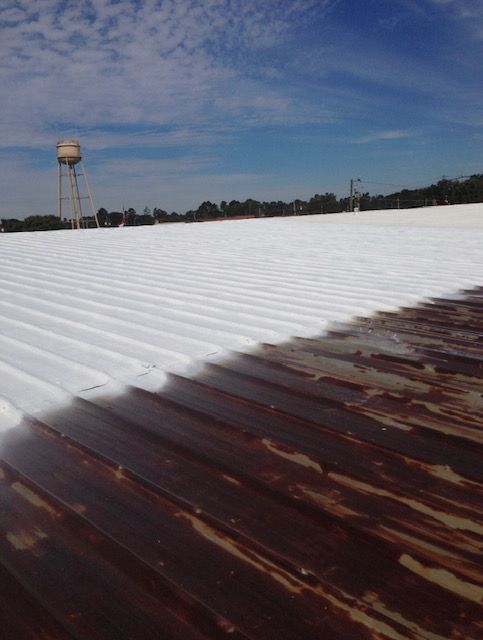 A roof is being painted white silicone coating, with a water tower in the background.