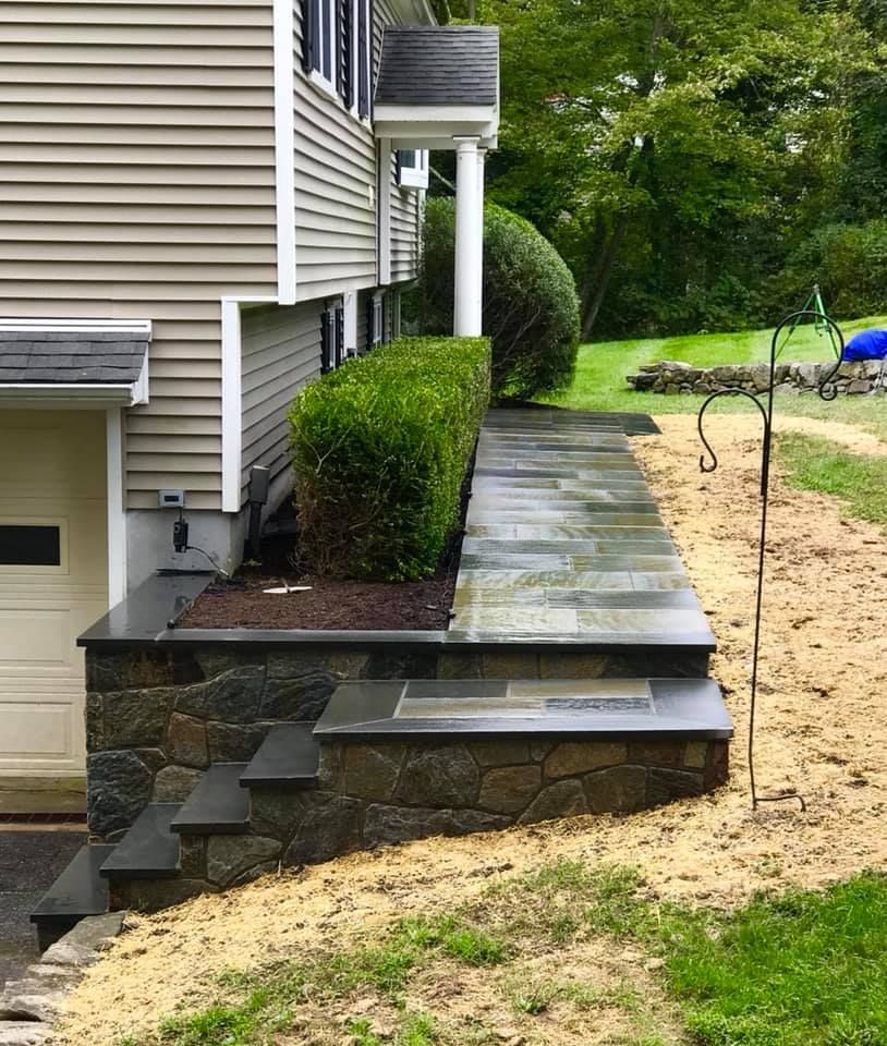 Stone steps and walkway alongside a beige house with green shrubbery.