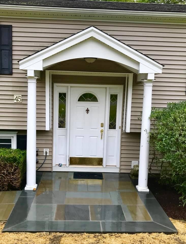 White front door with sidelights under a white portico, flanked by columns, on a gray tiled porch.