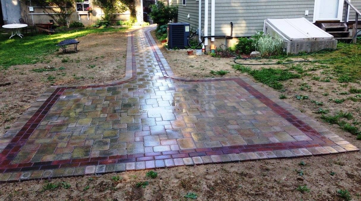 Brick patio and walkway with red border, in a backyard.