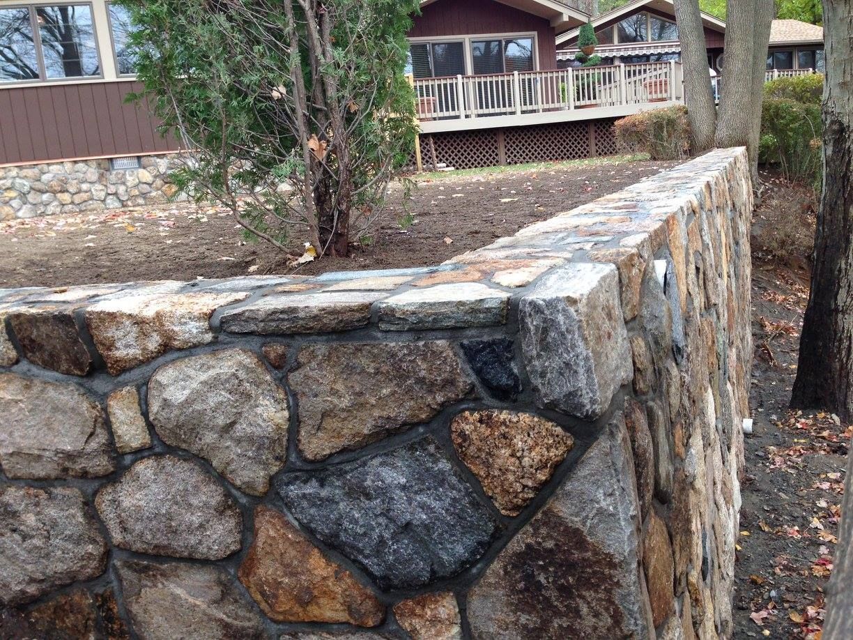 Stone retaining wall in front of a house with a deck, brown and gray stones.