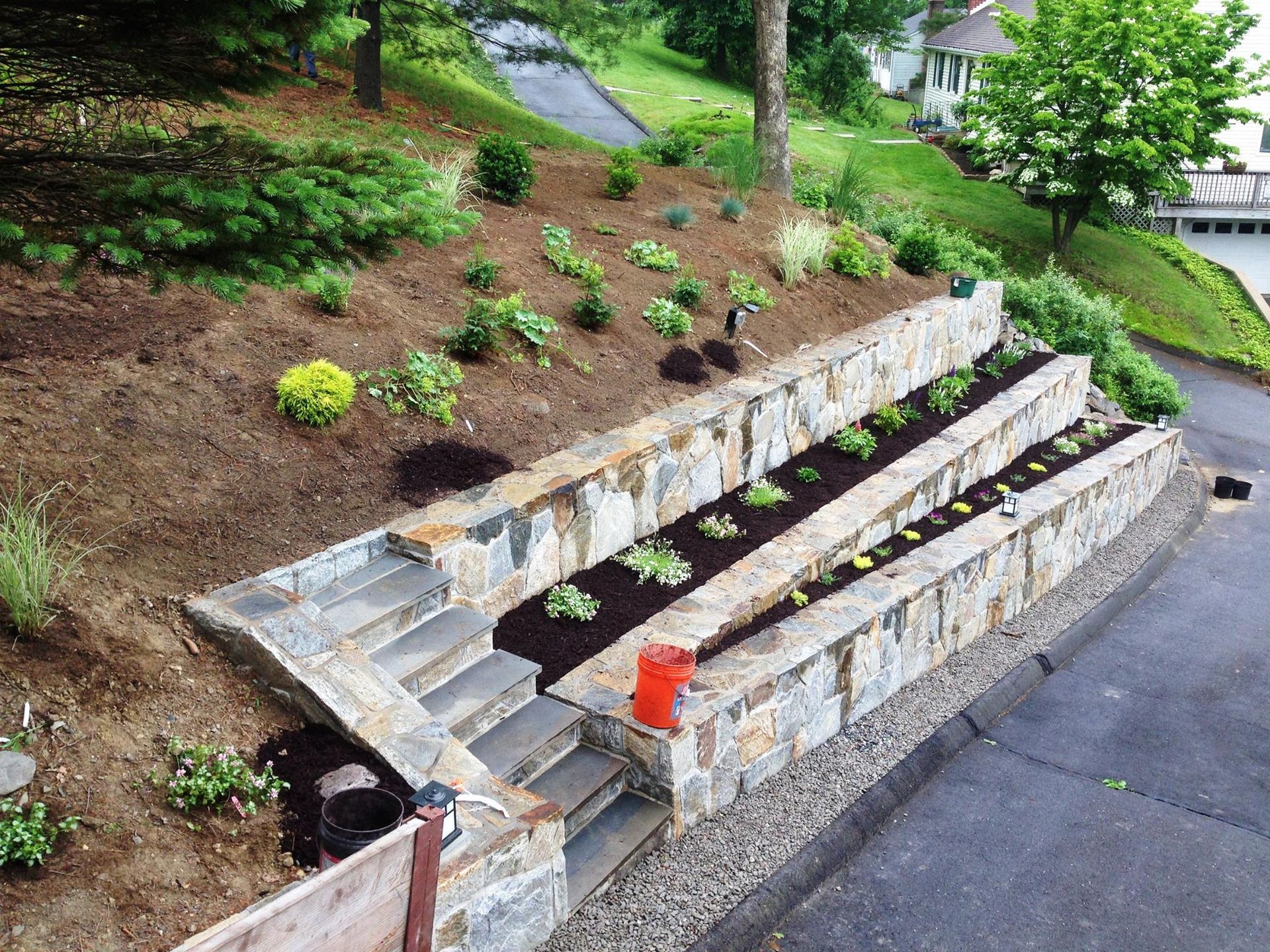 Stone tiered garden beds on a sloped hill with stairs, filled with plants.