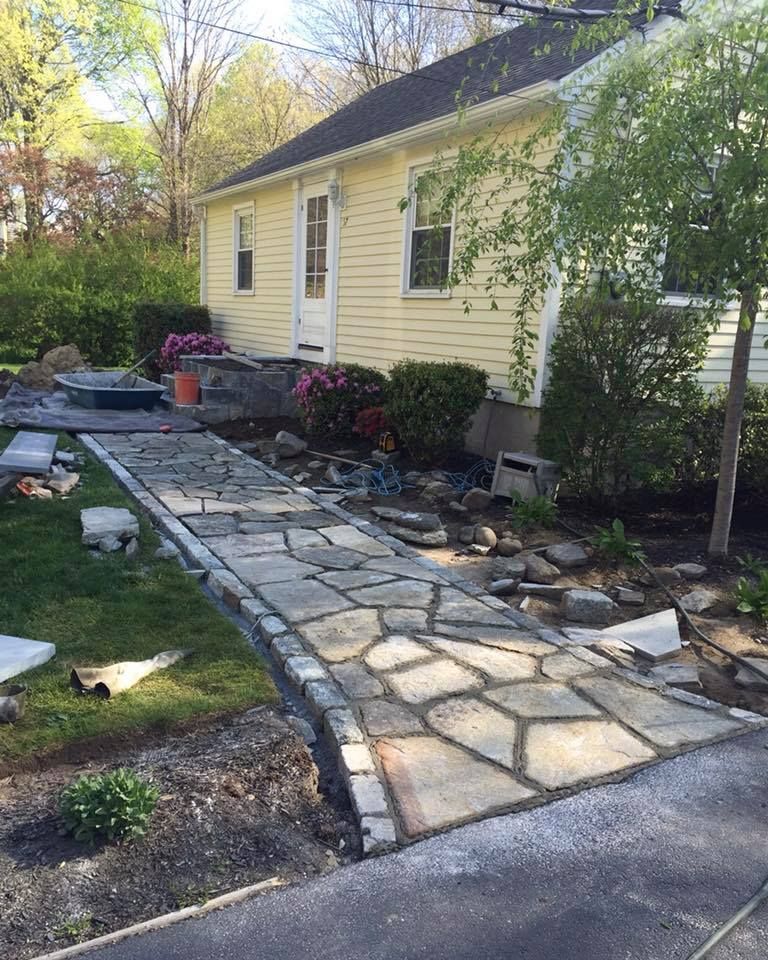 Stone walkway leading to a yellow house with landscaping and a small tree.