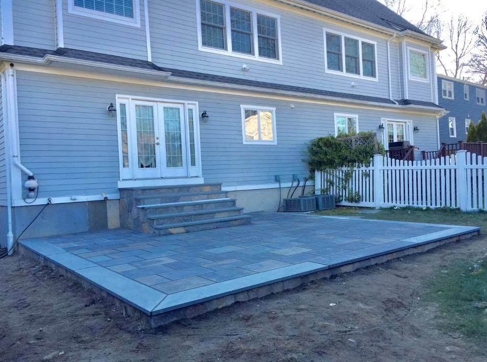 Backyard patio with steps leading to French doors, blue siding, white picket fence, and grass.
