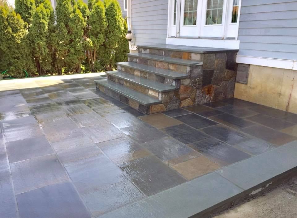 Blue-grey stone patio and steps leading to a white door; steps have a stacked stone side.
