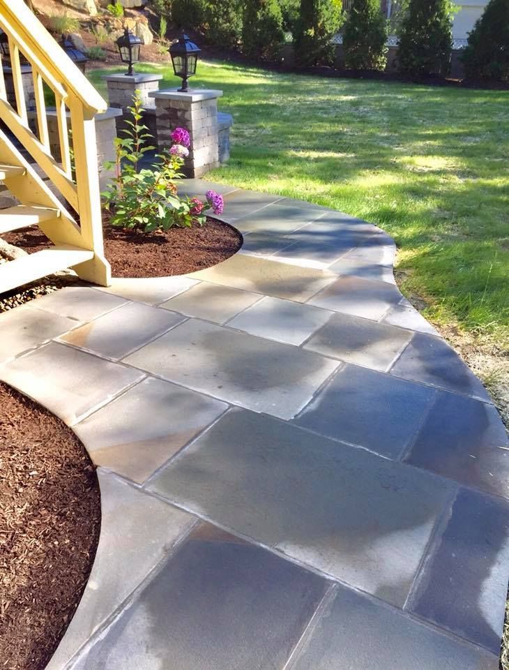 A stone pathway curves near a garden with a staircase and manicured lawn.