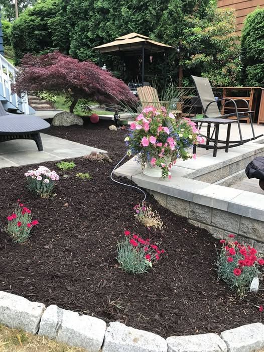 Flower garden with red and pink blooms next to a patio with furniture and a gazebo in the background.