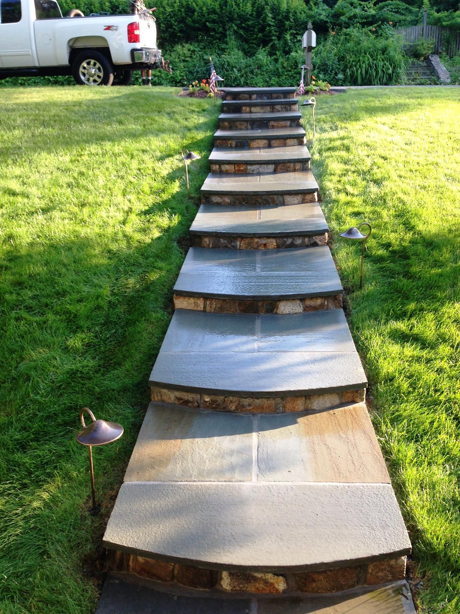 Stone steps lead uphill through grass, a truck visible in the background.