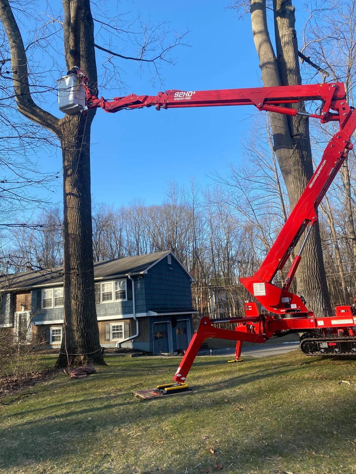 A red crane is cutting a tree in front of a house