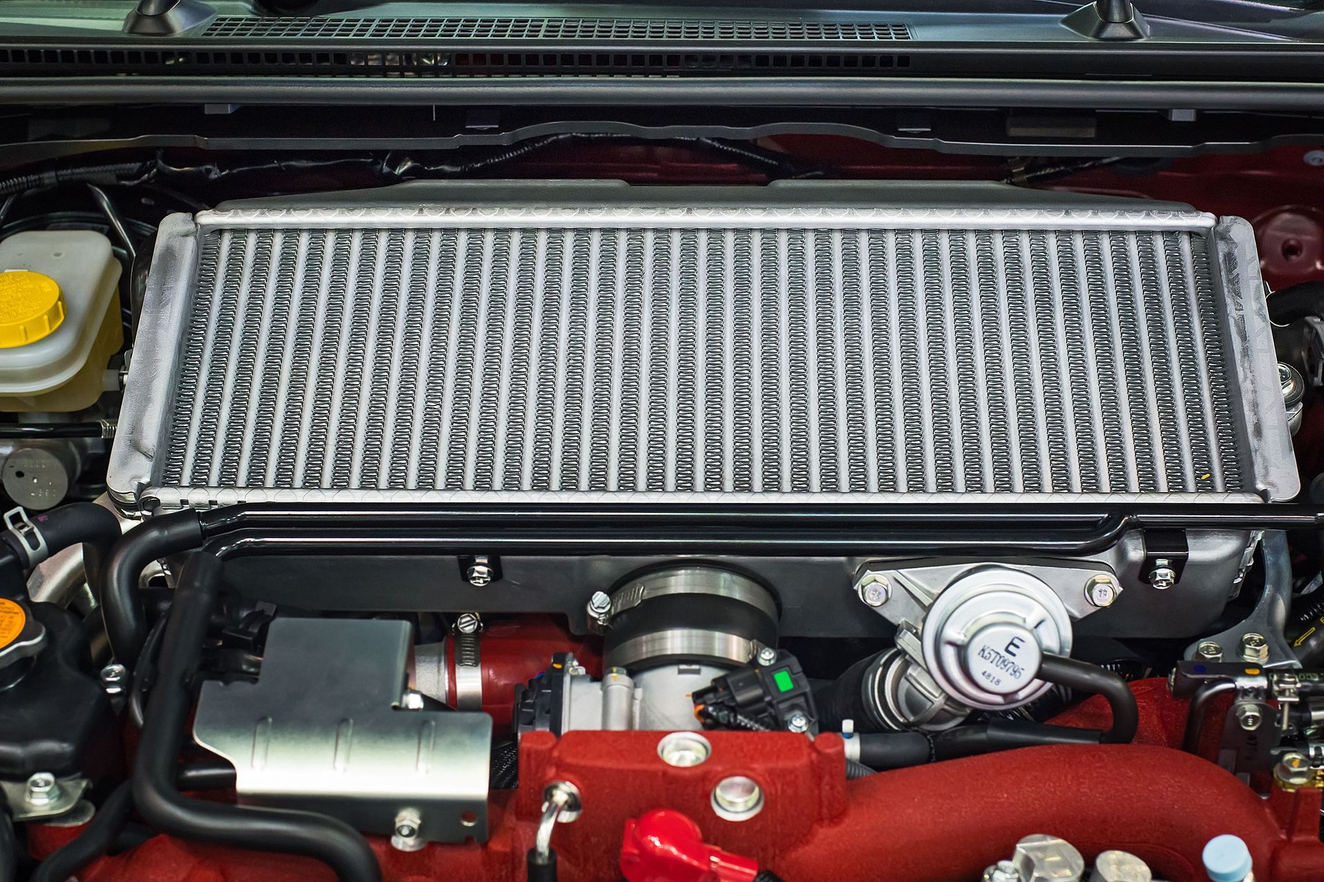 Top-mount intercooler in an engine bay. Silver radiator with black trim on red engine components.
