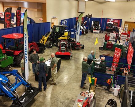 Indoor trade show with tractors, equipment booths, and people browsing displays