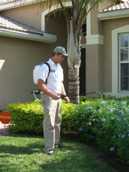 A man with a backpack spraying a lawn in front of a house