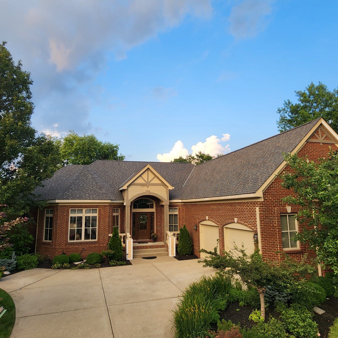 A brick suburban house with a two-car garage, a covered front entryway, and a concrete driveway under a blue sky.