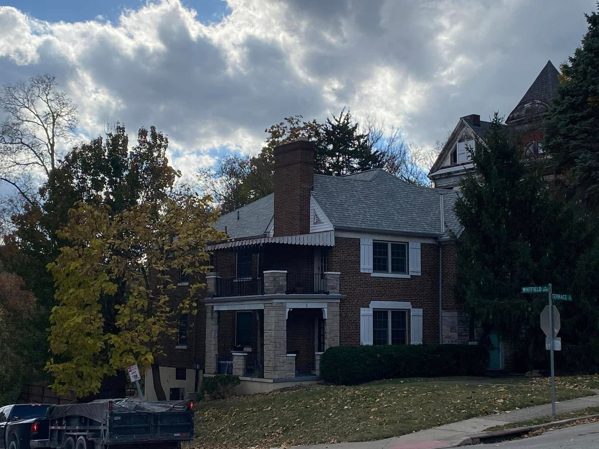 A brick house with a metal roof is surrounded by trees on a cloudy day