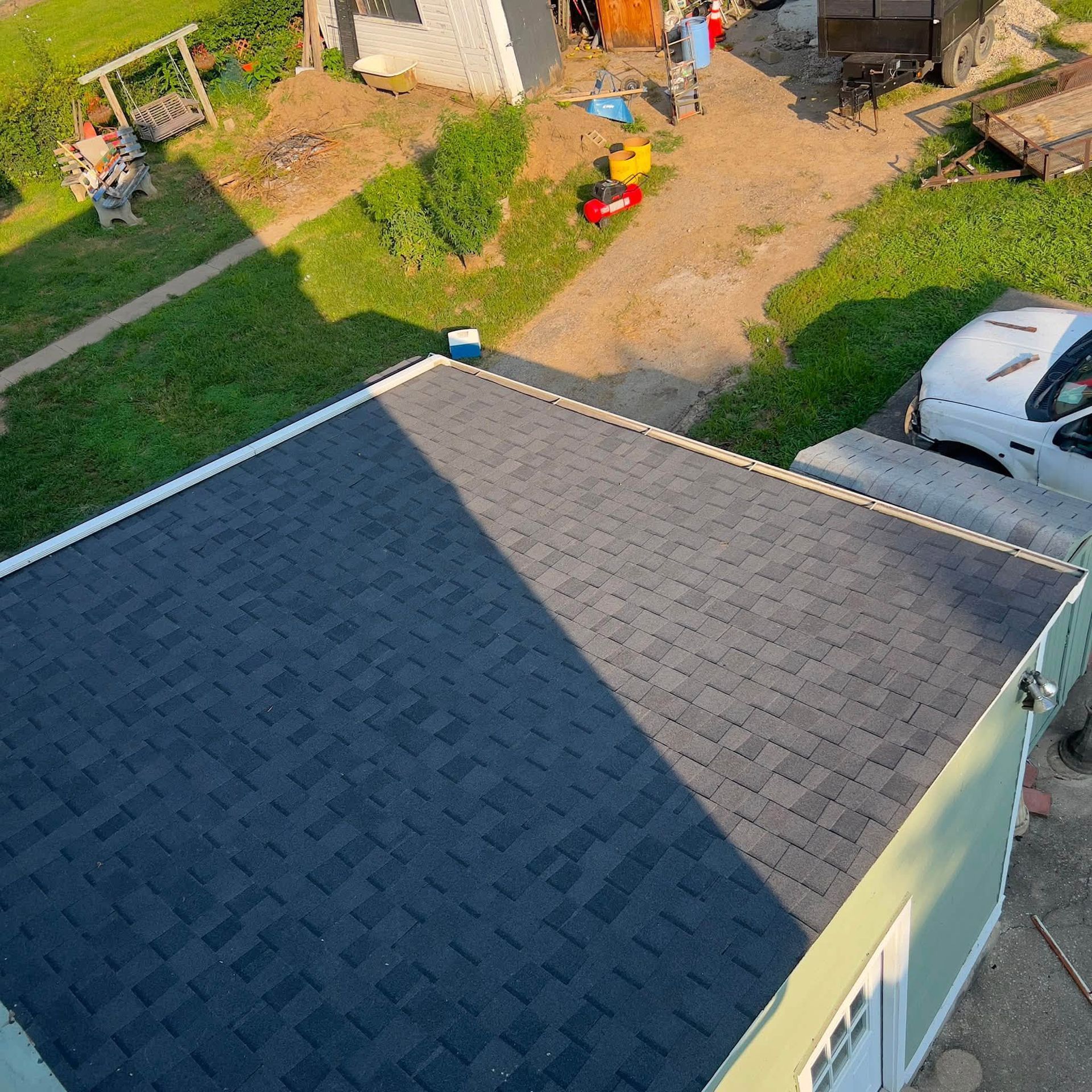 Backyard view with a dark shingled roof, driveway with white car, and children’s play area in the yard.