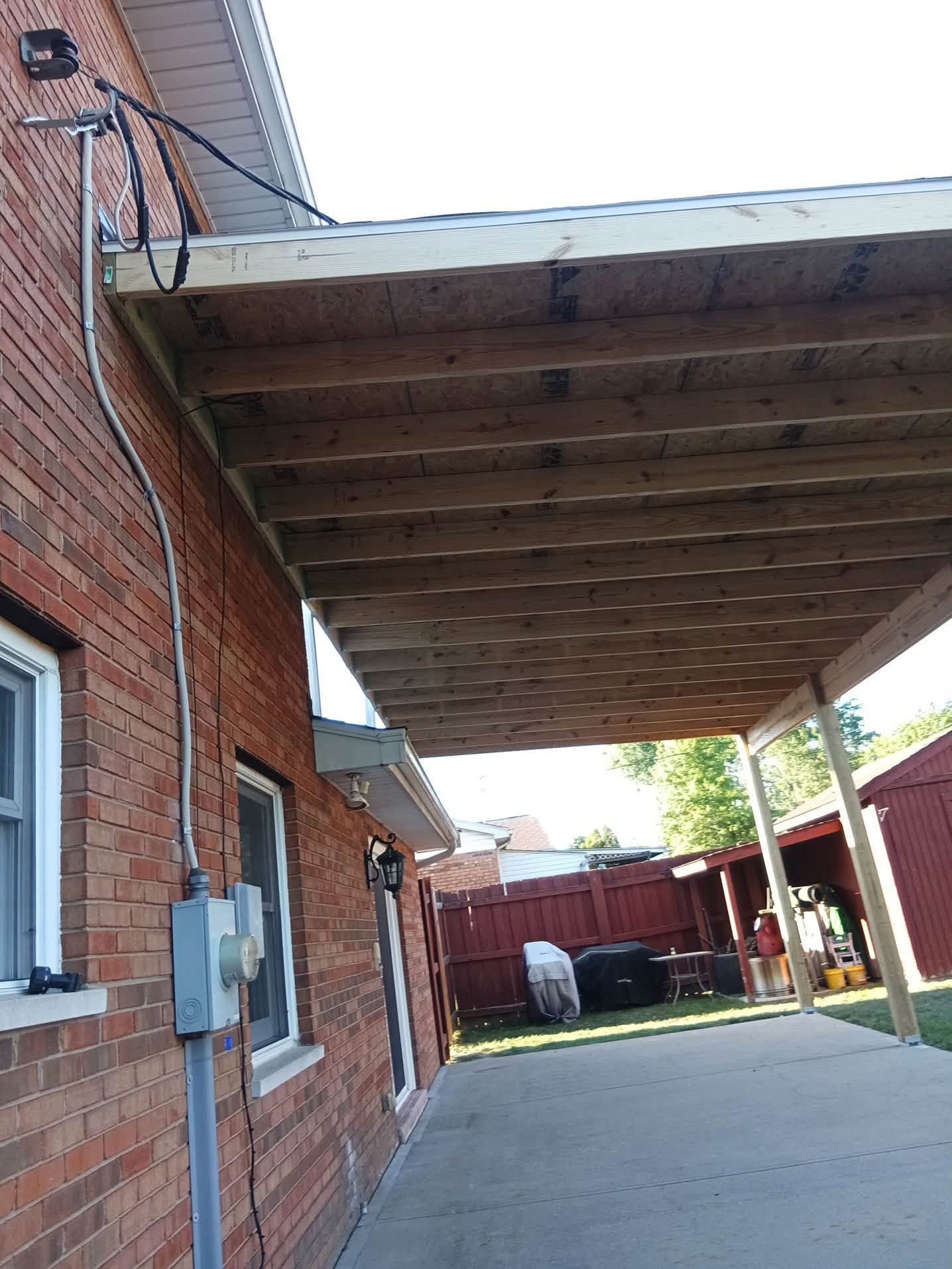 Covered patio beside a brick house with wooden beams and a concrete walkway leading to a fenced yard