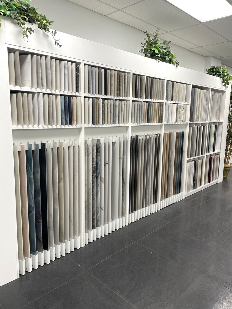Wall of neatly arranged fabric samples in a showroom, with white shelves and dark flooring.
