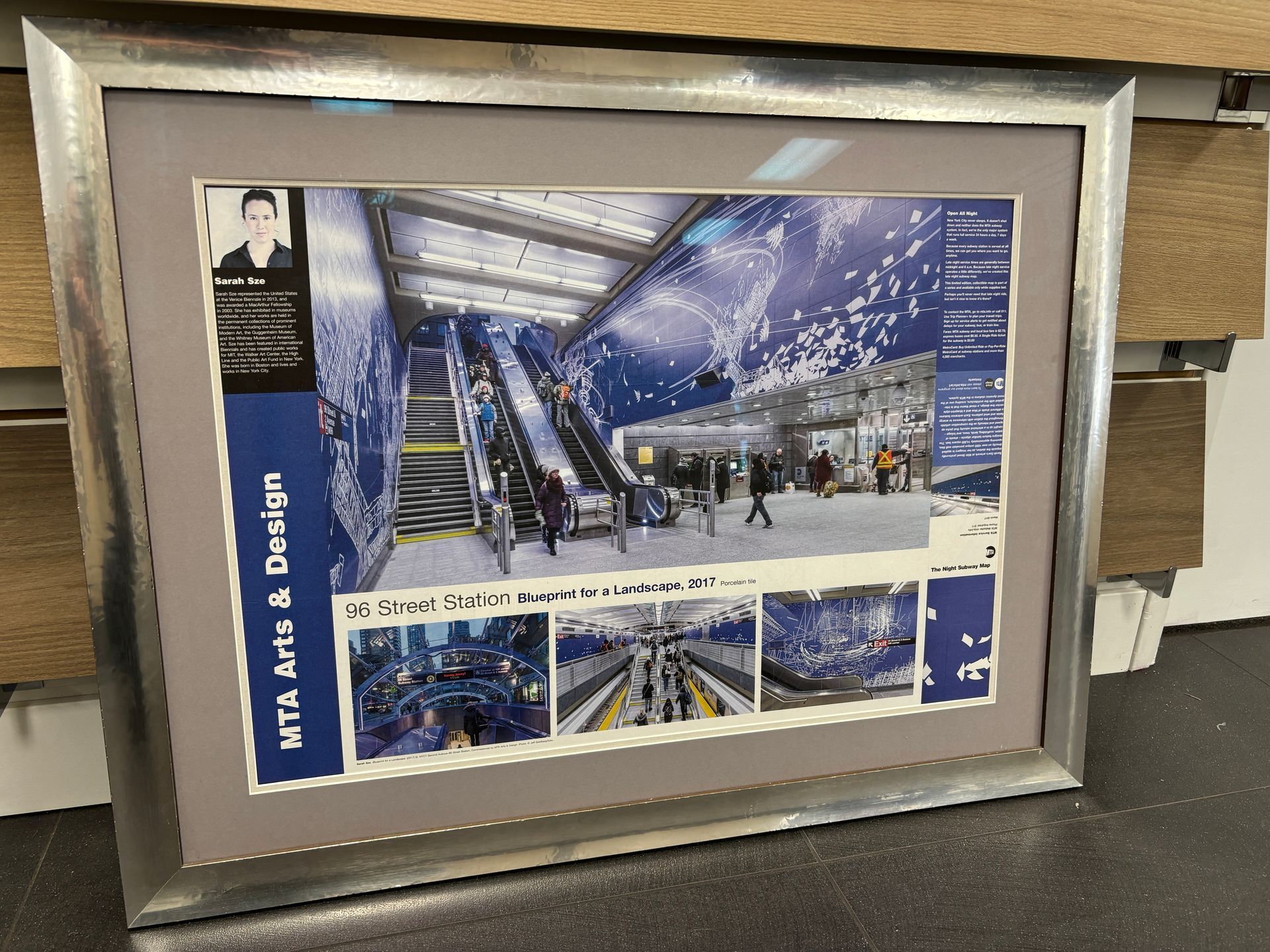 Framed concept art poster of a blue-lit airport or transit terminal with people and escalators