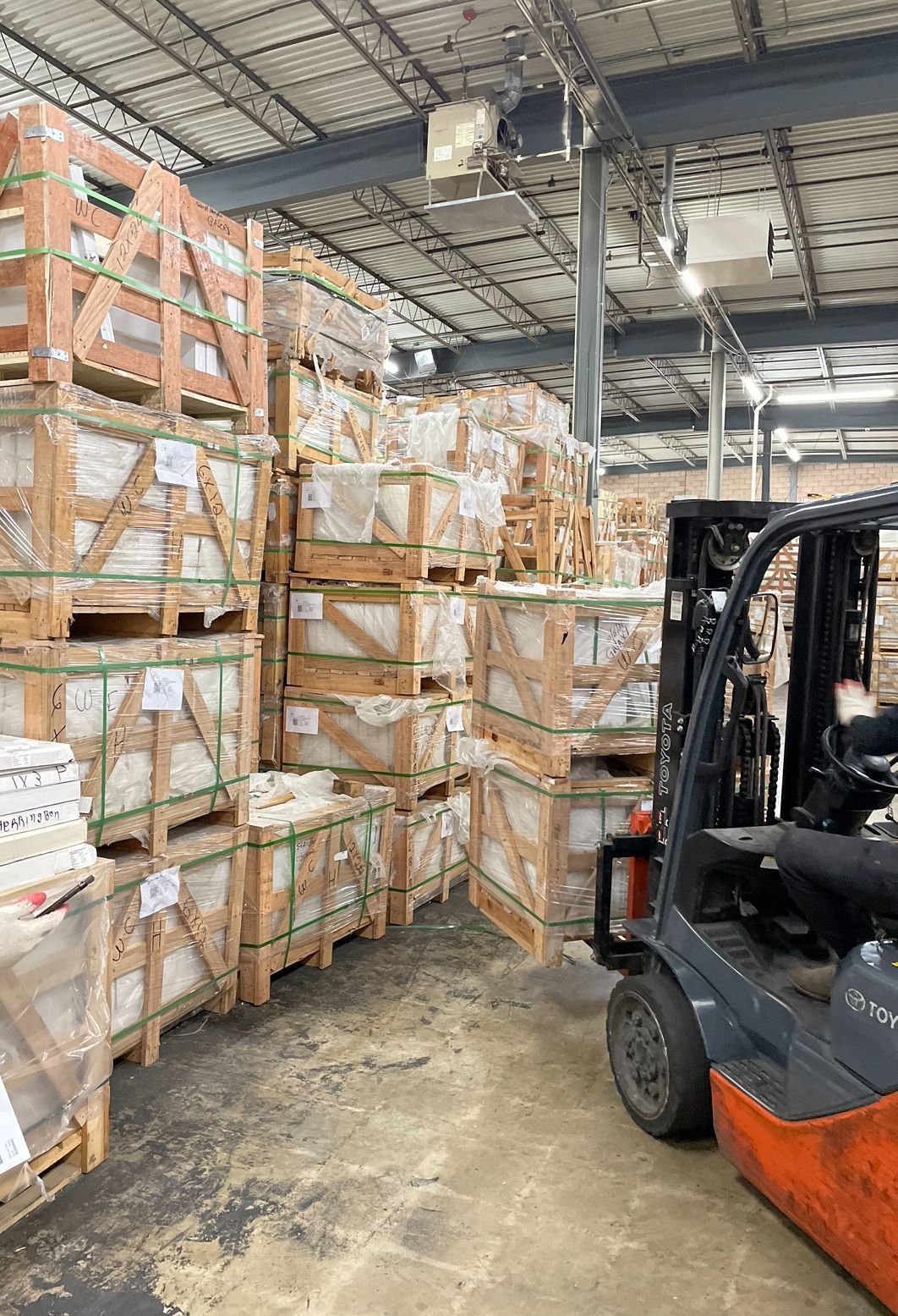 Warehouse aisle with stacked wrapped pallets and a forklift in the foreground