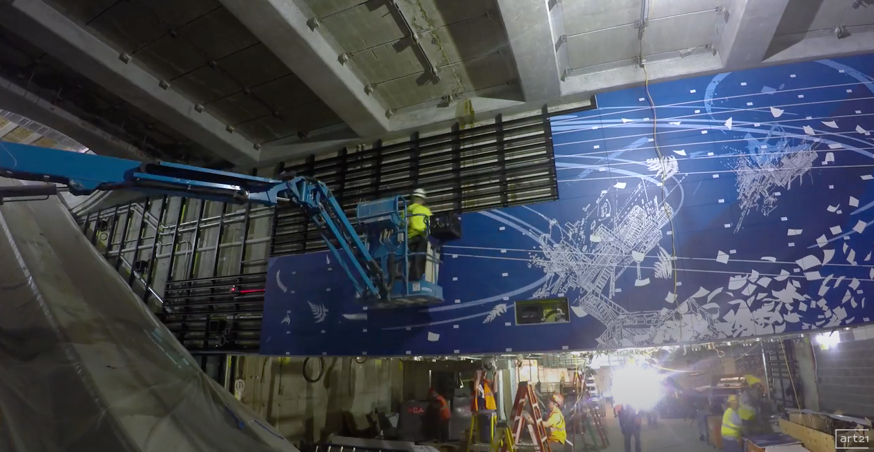 Workers on a blue indoor escalator maintenance platform in a stadium with a starry ceiling mural.
