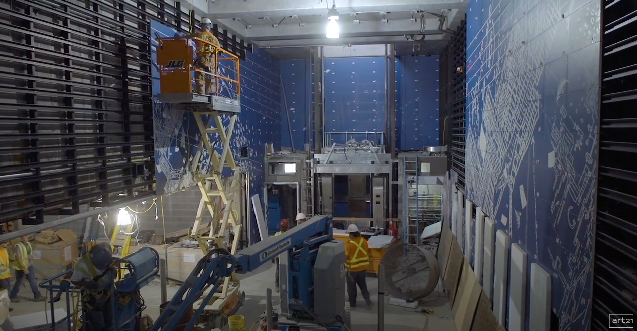 Industrial construction site with ladders, scaffolding, and blue wall panels under bright overhead lights