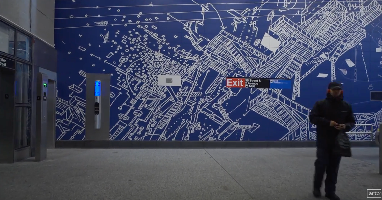 Indoor transit concourse with a blue map wall, elevator, exit sign, and a person walking in the foreground