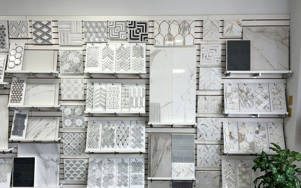 Wall display of tile samples in gray, white, and patterned designs, with shelves and a potted plant.