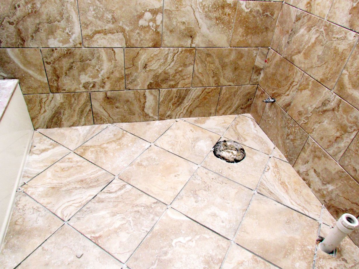 Partially tiled shower floor and walls with a drain and exposed plumbing pipe