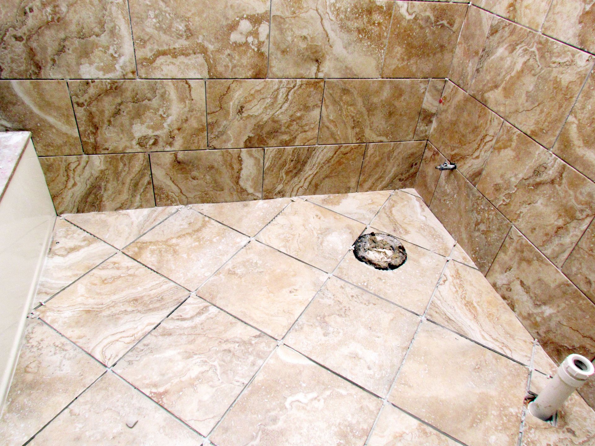 Partially tiled shower floor and walls with a drain and exposed plumbing pipe