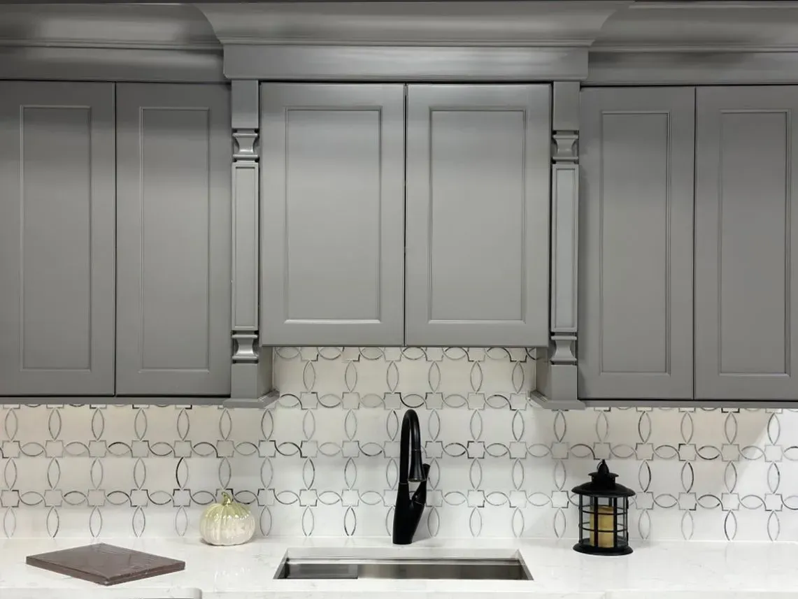 Gray kitchen cabinets with white hex tile backsplash, sink, and white countertop with decor accents