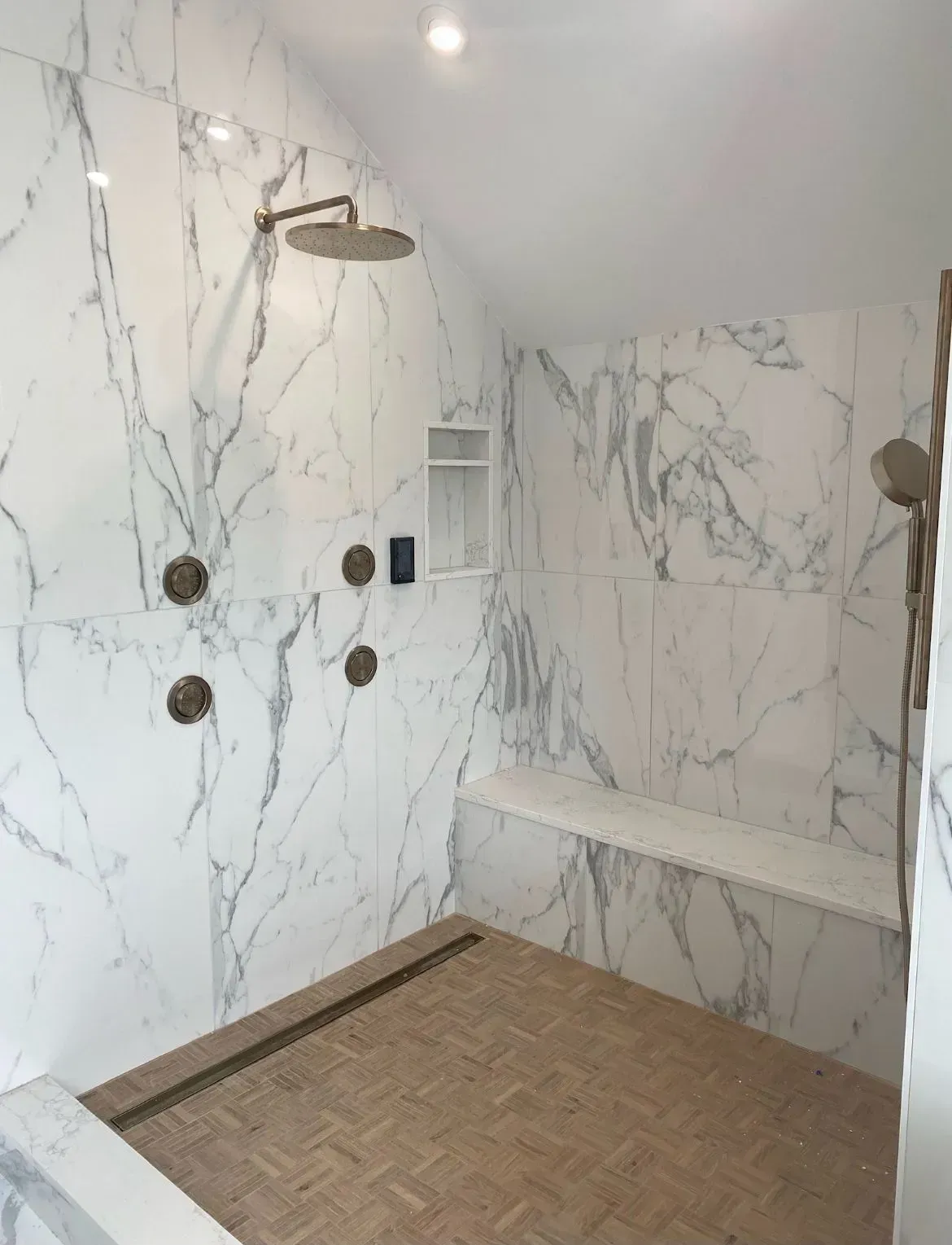 Marble-tiled bathroom shower with rain head, wall jets, and a woven floor mat