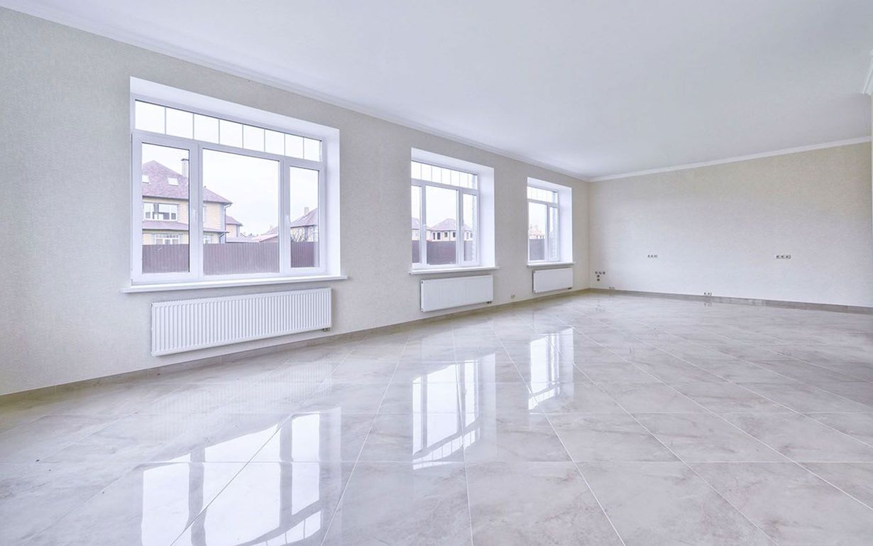 Empty bright living room with white walls, large windows, and glossy light gray floor.