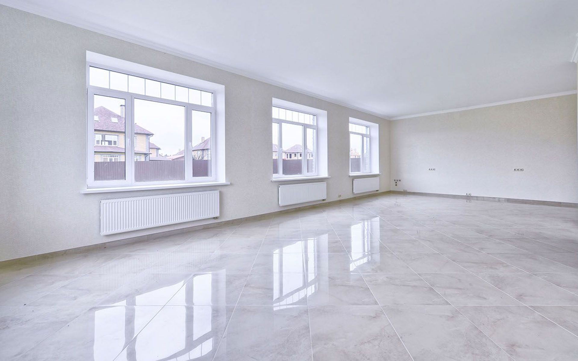 Empty bright living room with white walls, large windows, and glossy light gray floor.