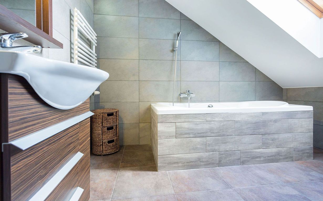 Modern bathroom with a freestanding tub, tiled walls, and a sloped ceiling.