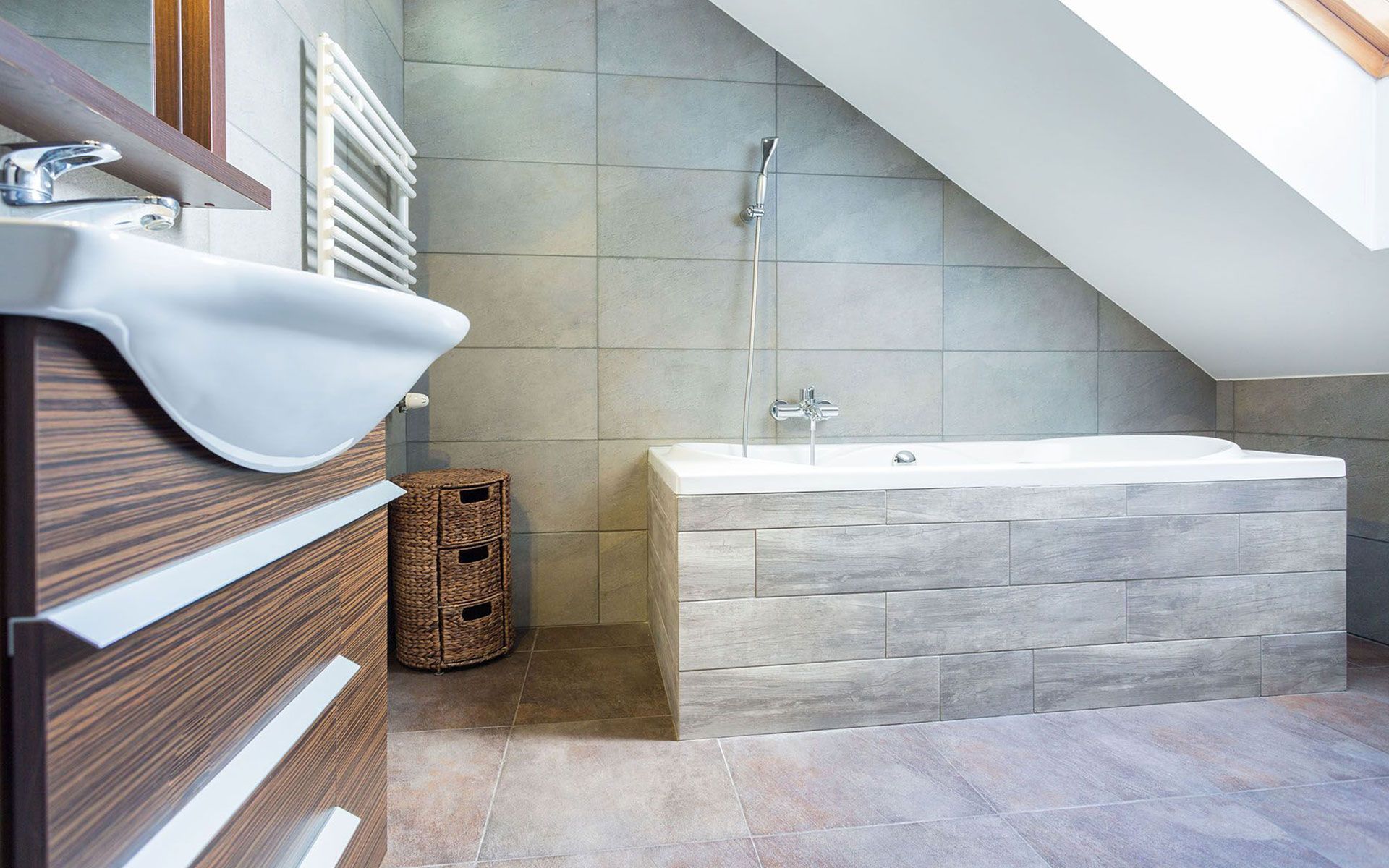 Modern bathroom with a freestanding tub, tiled walls, and a sloped ceiling.