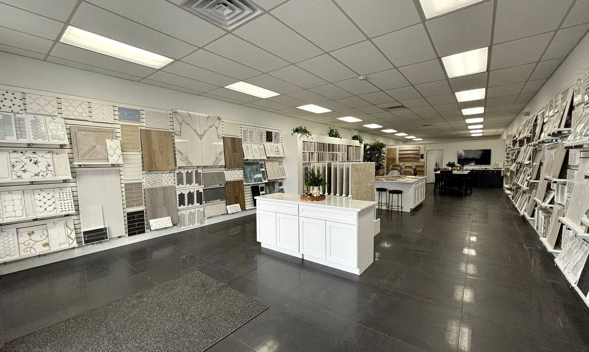 Bright showroom aisle with shelves of white kitchen cabinets and flooring samples under fluorescent lights