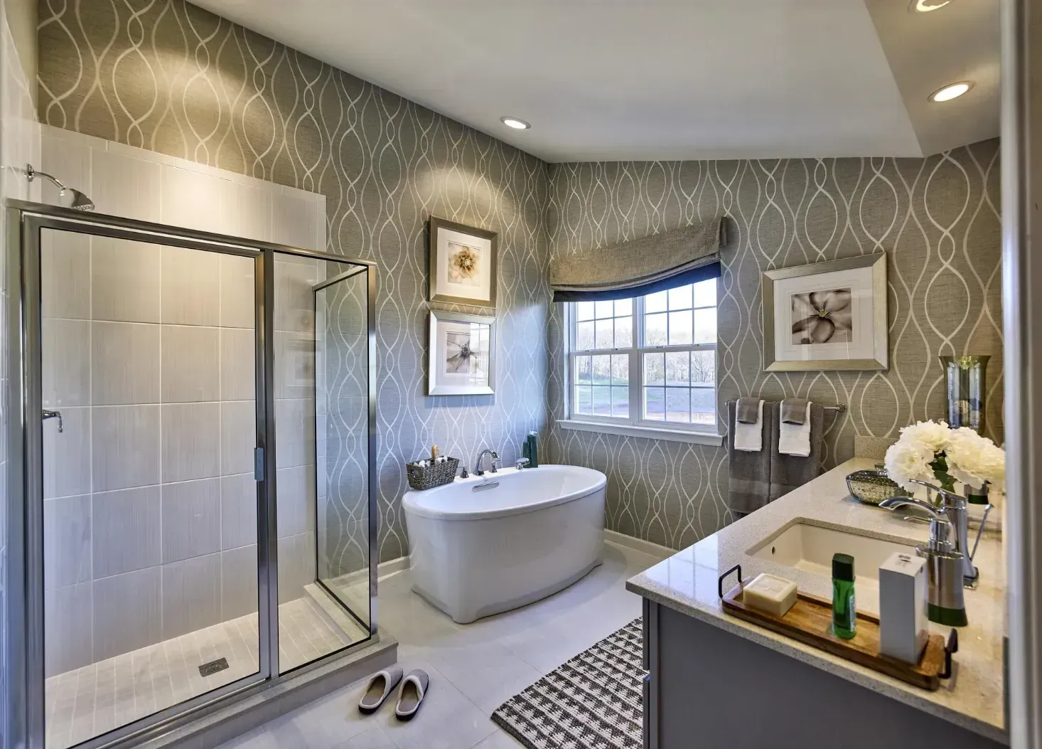 Modern bathroom with a glass shower, freestanding tub, vanity, and patterned wallpaper