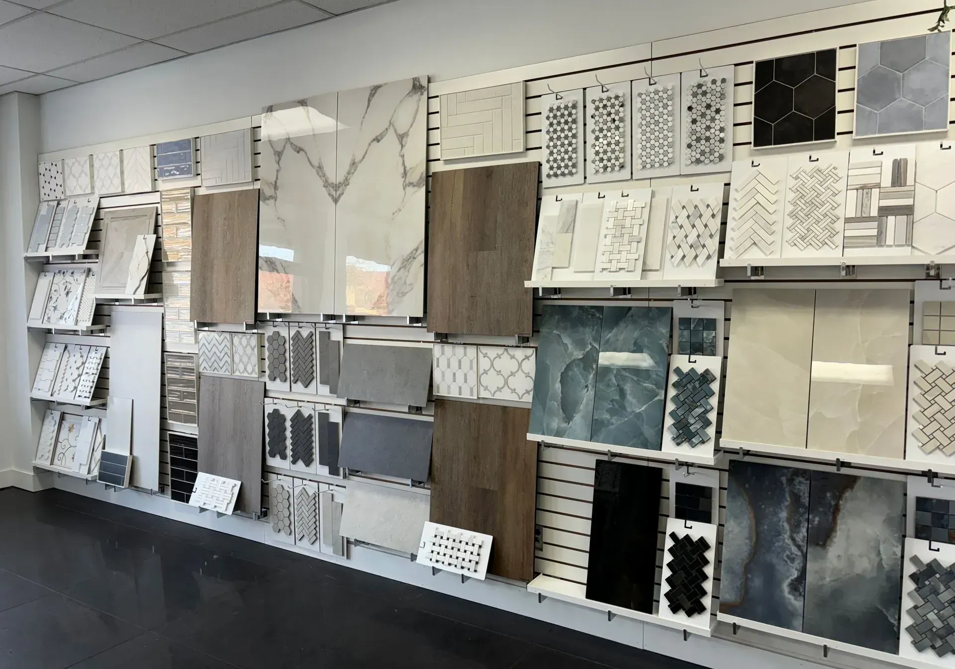 Display wall of assorted tile and stone samples in a showroom, showing colors, patterns, and textures.
